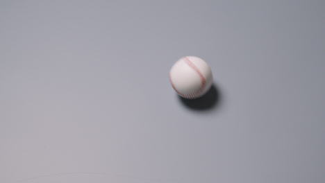 Overhead-Shot-Of-Baseball-Ball-Rolling-Across-Frame-Against-Grey-Background